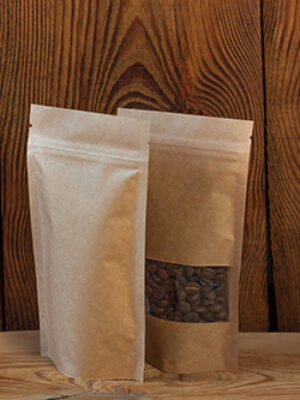 Brown kraft paper pouch bags with coffee beans front view on a wooden background. Packaging for foods and goods.